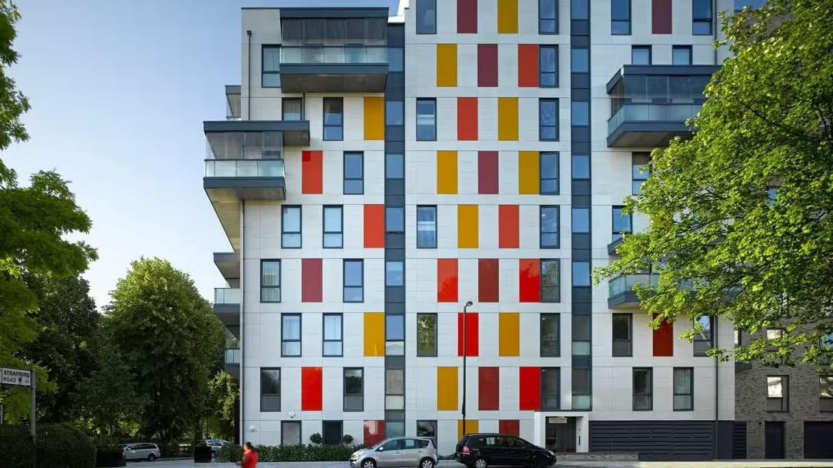 Duffy-Challenge Modern apartment building with red and yellow panels, balconies, and trees on both sides.