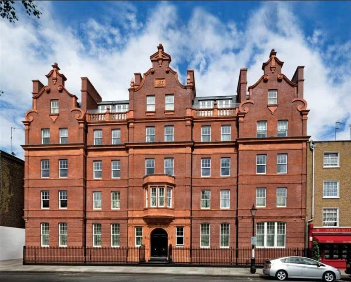 Duffy - Insights Red-brick building with ornate rooflines, many windows, and a car parked in front on a city street.