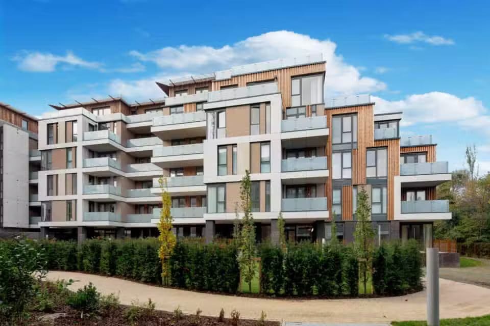 Duffy-Managing Modern apartment building with balconies, landscaped bushes, and a clear blue sky in the background.