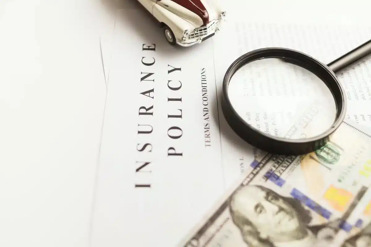Insurance policy document with a magnifying glass, toy car, and a $100 bill.