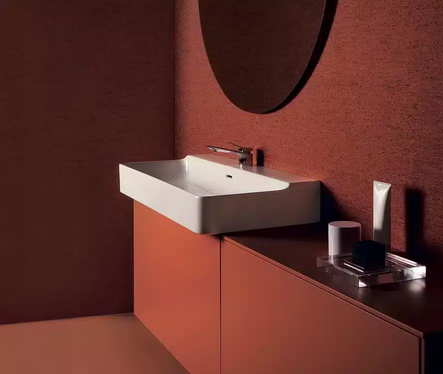 Modern bathroom with a white rectangular sink, round mirror, and brown cabinets against brown walls.