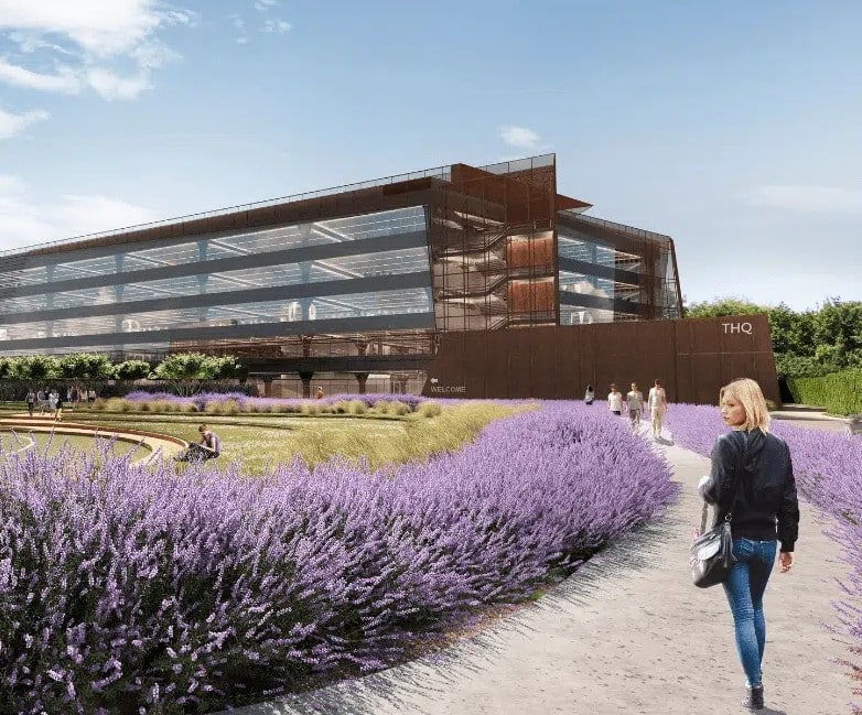THG-HQ People walk along a path surrounded by purple flowers near a modern glass and steel building.