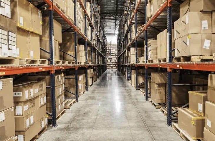 THG-Warehouse Warehouse aisle with shelves stacked with cardboard boxes.