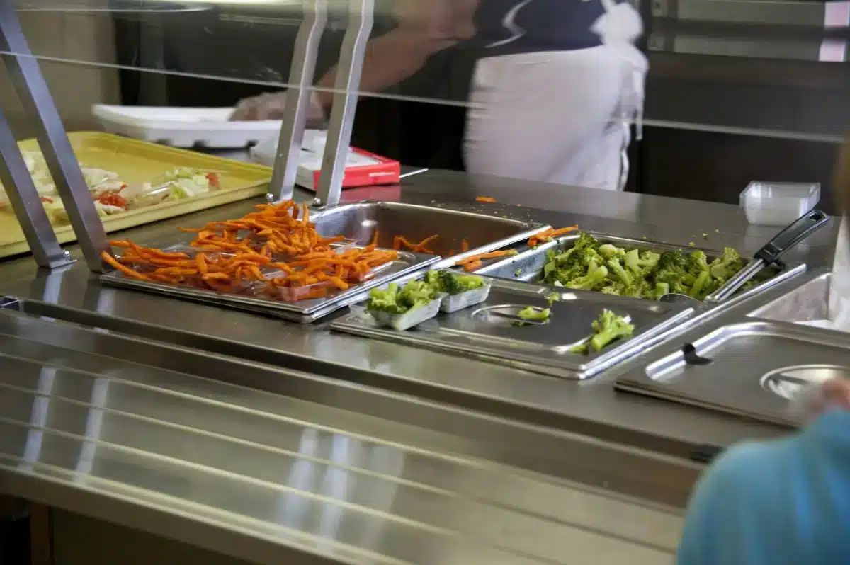 TonbridgeSchool-Work A cafeteria food counter with trays of carrots and broccoli behind a glass shield.