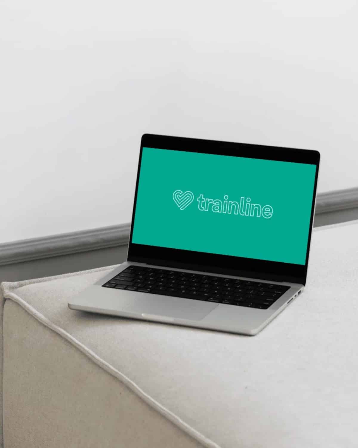 Trainline - The Challenge A laptop on a cushioned surface displays the Trainline logo on its screen.