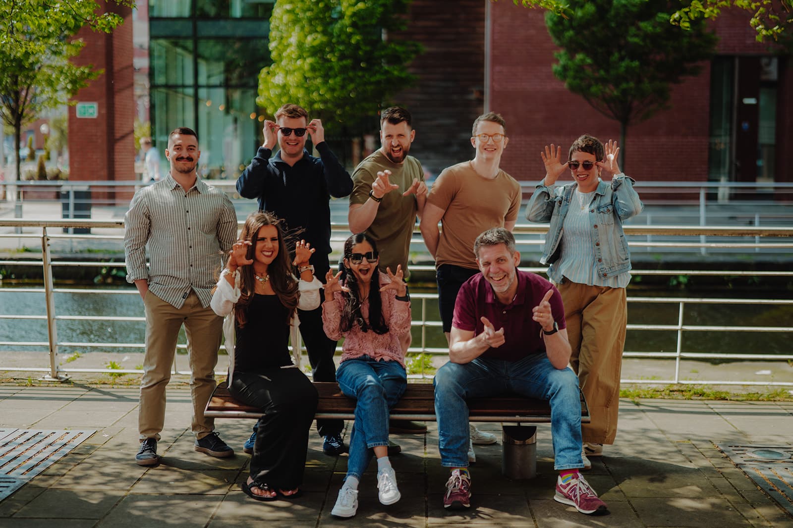 MY CARBON Group of people posing playfully outdoors, some making funny faces and hand gestures.